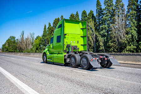 Industrial grade professional use bright green powerful big rig semi truck tractor without the semi trailer running on the wide highway road to warehouse for picking up the next freight loadの写真素材