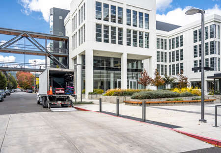 White middle class relocation rig day cab semi truck tractor with long spacious box trailer standing on the urban city street with multilevel apartment and office buildings unloading delivered goodsの写真素材