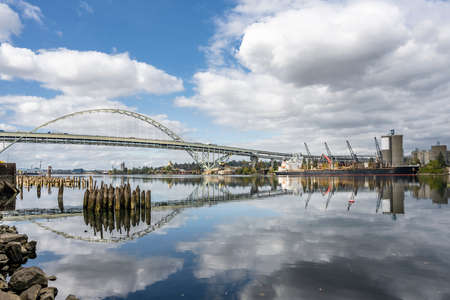 Autumn Landscape with transportation double-story Fremont Bridge with big arched support over the Willamette River in Portland with water reflection and remnants of the piles of the old pierの写真素材