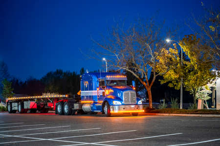 Blue big rig semi truck tractor with sleeping compartment in high roof cab for truck driver rest and with dry van semi trailer standing for rest on the industrial truck stop parking lot at night timeの写真素材