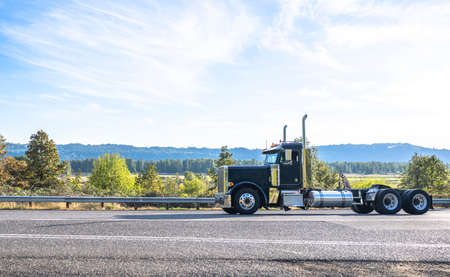 Industrial powerful black big rig semi truck tractor without semi trailer driving on the winding narrow road through the autumn forest in Columbia Gorge area to warehouse for pick up next loadの写真素材