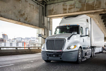Popular bonnet powerful big rig semi truck tractor with high cab for long haul freights transporting commercial cargo driving on two level arched Fremont bridge across Willamette river in Portlandの写真素材
