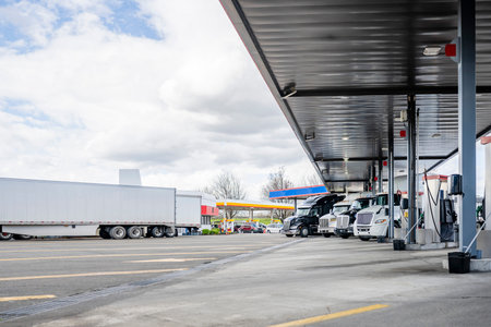 Long haul big rigs semi trucks with semi trailers standing on the truck stop fuel station refueling...