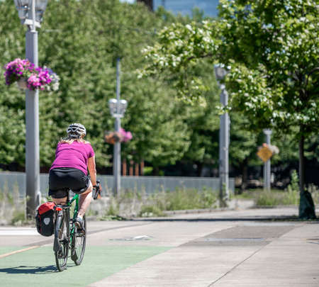 Slender woman on a bike rides a bicycle along the concrete city sidewalk  preferring an active healthy lifestyle using cycling ride and cycle as an alternative environmentally friendly transportationの写真素材