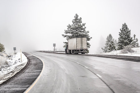 Broken big rig semi truck with open hood and semi trailer standing out of service on the winter road with snow storm waiting for towing truck or diagnostic technician inspection and quick repairの写真素材