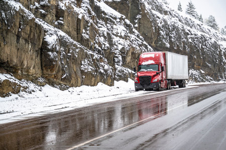 Red big rig commercial semi truck transporting cargo in dry van semi trailer standing out of road on the top of mountain pass at at snowing weather during a snow storm near Shasta Lake in Californiaの写真素材