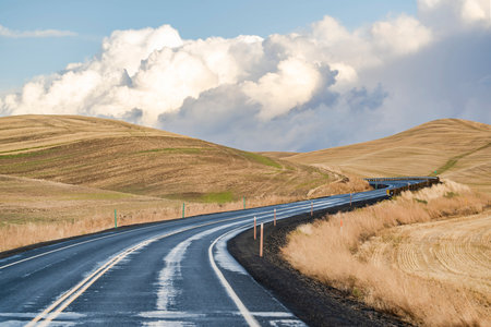 Scenic autumn landscape with a winding narrow highway road lost between the hills with hay-cut grass...