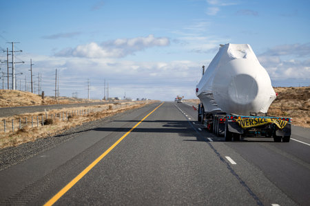 Industrial gray classic big rig semi truck tractor with oversize load sign and step down semi trailer transports oversized covered and fastened cargo driving on the highway road in Columbia Gorgeの写真素材