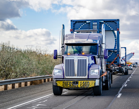 Industrial blue big rig semi truck tractor with additional trolley transports oversize load a super long blade of a wind turbine with an escort car driving on the highway road in Columbia Gorgeの写真素材
