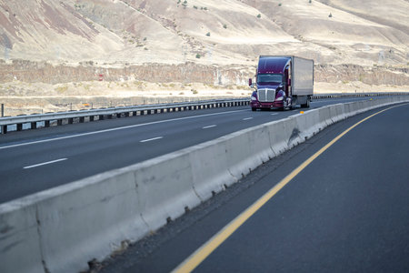 Industrial big rig purple semi truck tractor with high cab transporting cargo in dry van semi trailer driving on divided highway road along the river with electric wind turbines in Columbia Gorgeの写真素材