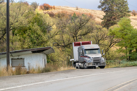 Industrial standard gray big rig semi truck with dry van semi trailer standing on the driveway to the house on the downhill side of the highway waiting for the next commercial flightの写真素材