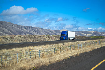 Industrial standard big rig pearl blue semi truck tractor with roof spoiler transporting cargo in dry van semi trailer driving on straight mountain highway road along the river in Columbia Gorgeの写真素材
