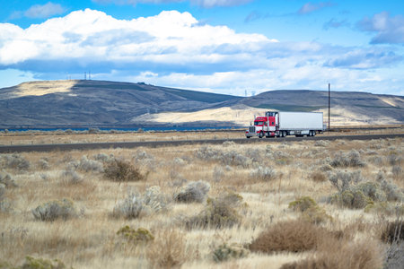 Industrial standard long hauler big rig red semi truck tractor transporting cargo in refrigerator semi trailer driving on divided highway road along the the meadows in Columbia Gorgeの写真素材