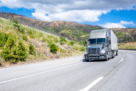 Industrial long hauler big rig gray semi truck tractor with grille guard and extended cab for truck driver rest transporting commercial cargo in dry van semi trailer driving on road at sunny dayの写真素材