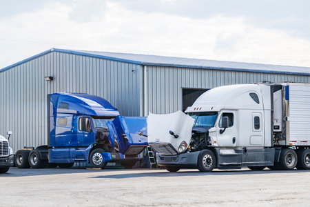 Bonnet industrial freight broken big rig semi trucks with open hoods standing on the parking lot of the repair shop for engine maintenance and inspection and necessary current repairsの写真素材