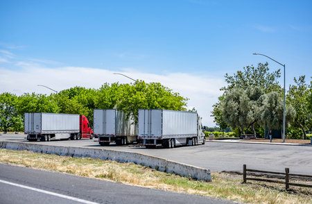 General logistic transportation different long haulers big rigs semi trucks with semi trailers standing in row on truck stop parking lot for truck driver rest waiting for the continuation freightsの写真素材