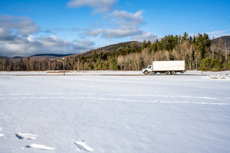Industrial commercial compact middle duty rig white day cab semi truck tractor transporting cargo in box trailer driving on the slippery winter city road in New England making local deliveriesの写真素材