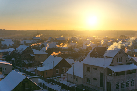 Aerial view on winter village landscape with snow covered roofs, blue sky and sunrise in the morning. Snow houses with smoke out of chimney in winter dreamland at dawn. Ukraine, Irpinの写真素材