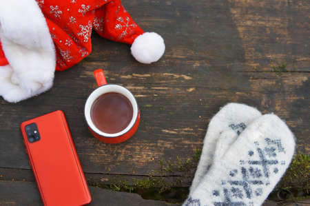 a red smartphone mittens and a mug of tea are on the wooden tableの写真素材