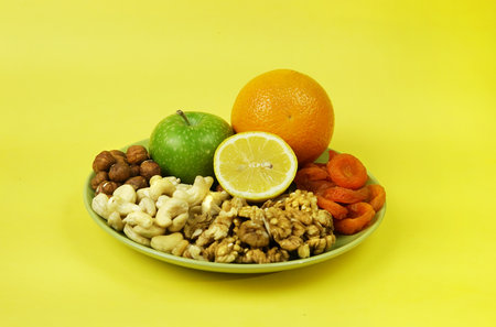 plate with nuts orange on a yellow background hazelnuts walnuts cashews dried apricotsの写真素材