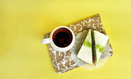 a colored cake and a cup of tea on a napkin on a yellow background on theの写真素材