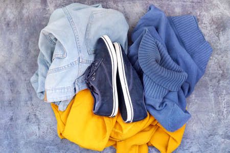 clothes on blue background: jeans blue sweater yellow hoodie sneakers. Top viewの写真素材
