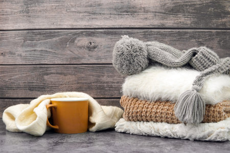 Beige mug wrapped in a white scarf and winter clothes on the tableの写真素材