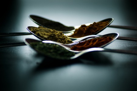 Spices colored in silver spoons, placed on a black wooden table. Pepper, pepper, salt, basil, mustardの写真素材