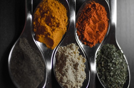 Spices colored in silver spoons, placed on a black wooden table. Pepper, pepper, salt, basil, mustardの写真素材