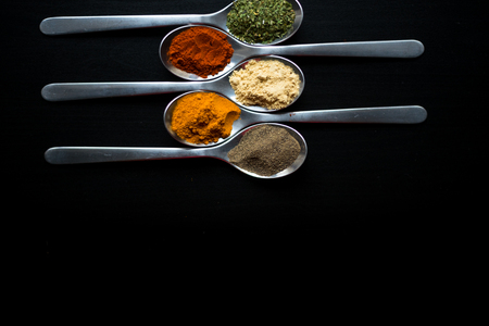 Spices colored in silver spoons, placed on a black wooden table. Pepper, pepper, salt, basil, mustardの写真素材