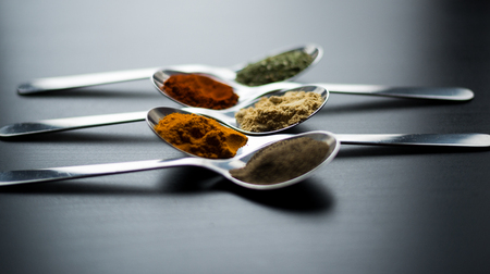 Spices colored in silver spoons, placed on a black wooden table. Pepper, pepper, salt, basil, mustardの写真素材