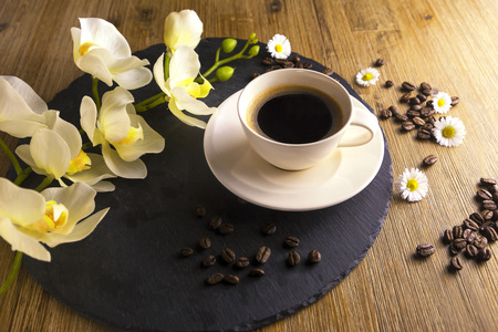 Composition made from cup of black tea with a black and brown background. Cup of black coffee with white flower, chamomile and coffee beans. It simbolizes nice morning with tasty tea.の写真素材