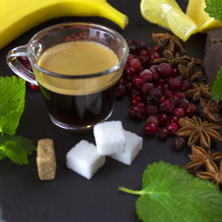 Exposition close up of fresh organic fruit and chocolate with coffee cup, chili pepper, half of lemon, sliced ??ââbanana, mint leaf, cinamone, blackberry and coffee grape on black background, rock boardの写真素材