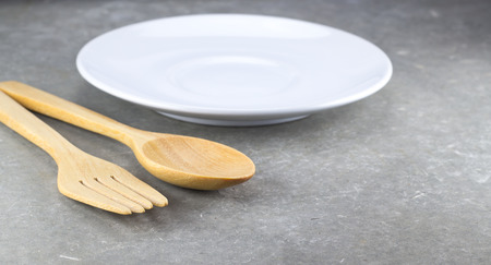 wood spoon and fork with white dish on cement tableの写真素材