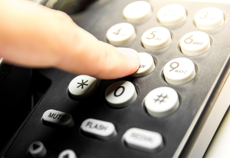 Finger press number button keypad on black telephone for call in flare light warm tone theme.の写真素材