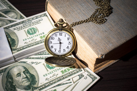 Still life image of pocket watch on bills and old book