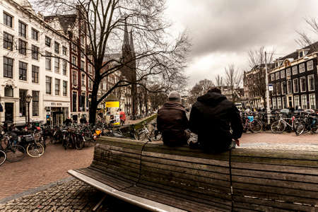 Amsterdam, The Netherlands - February 26, 2010: People sitting on the top of the bench and looking on Amsterdam canal.のeditorial素材