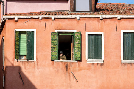 Italy, Florence - March 11, 2012: Old man looking through the window in ancient Italian house.のeditorial素材
