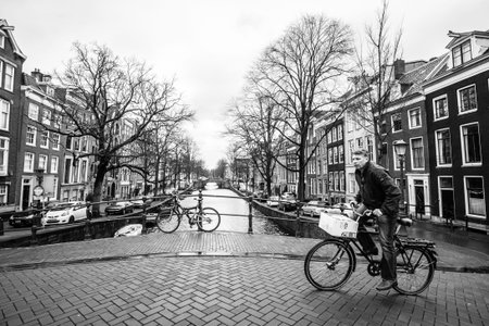 Amsterdam, The Netherlands - February 26, 2010: Man rides a bicycle on the street near water canal. Bicycle is very popular transport in Amsterdam.のeditorial素材