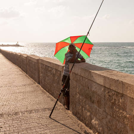 Tel Aviv, Israel - September 9, 2011: Adult man fishing under the umbrella in the Tel Aviv Promenade.のeditorial素材