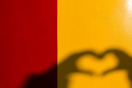 Silhouette of heart-shape hand on the bright yellow and red background.の写真素材