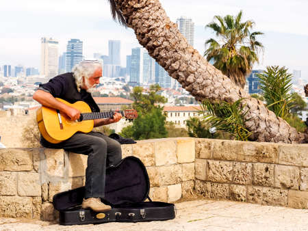 Jaffa, Israel - February 4, 2017: An elderly street musician playing the guitar against the background of skyscrapers of Tel Avivのeditorial素材