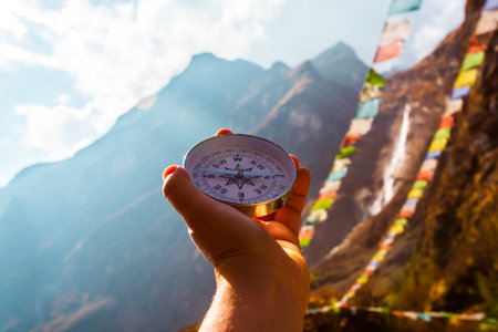 Round compass in hand on the background of blurred mountain and prayer buddhist flags fluttering in...