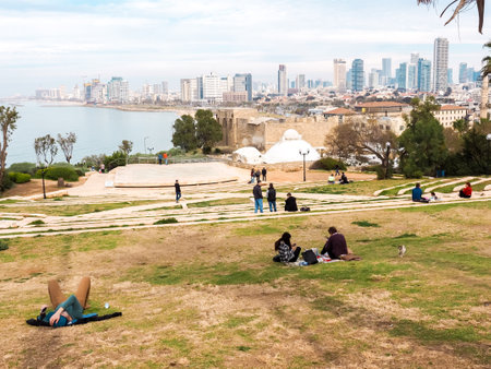 Jaffa, Israel - February 4, 2017: People relaxing on the lawn and admiring the view of the Tel Aviv promenade with modern skyscrapers along the seacoast.のeditorial素材
