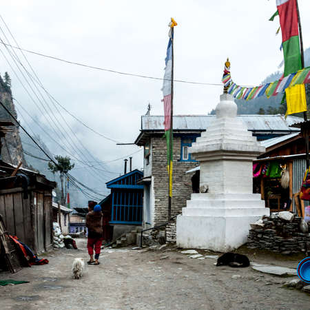 Chame, Nepal - November 7, 2015: Old woman with child on the back going down the street in the mountain village in Nepal, Himalayaのeditorial素材