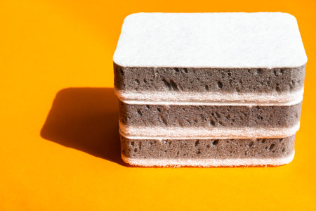 Three grey kitchen sponges on the orange background, cleaning conceptの写真素材