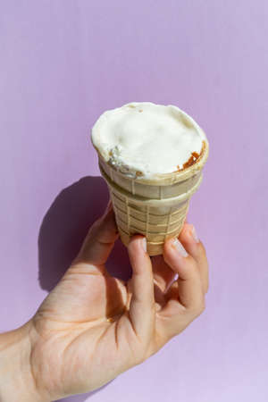 Hand holding an ice cream cone on the purple background. Summer conceptの写真素材