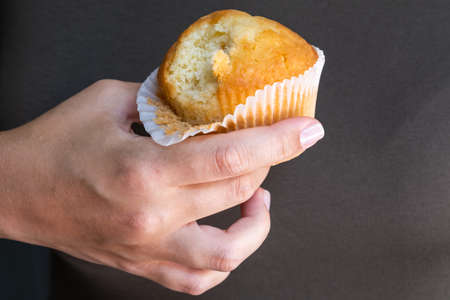 Female hand with tasty cupcake on the brown background, junk food conceptの写真素材