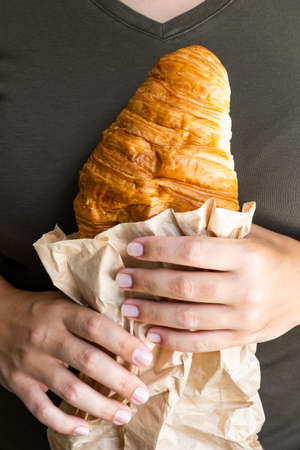 Female hands holding tasty croissant on the brown background, junk food conceptの写真素材