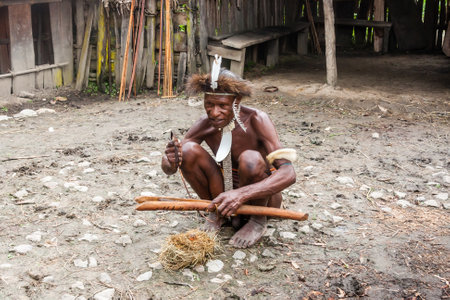 Wamena, Indonesia - January 9, 2010: Man of the Dani tribe in a traditional dress kindles fire. Baliem Valley Papua, Irian Jaya, Indonesian New Guineaのeditorial素材